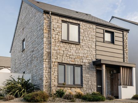 A stone house with windows and a small garden in front at Driftwood in Crantock