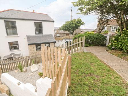 A garden with a wooden fence and gate lawn shrubbery and a paved pathway next to a white house at Rose Bank Cottage in St Just