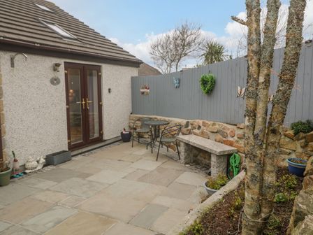 An outdoor patio area with a stone bench metal chairs and table potted plants and decorative wall at Pippas place in St Just
