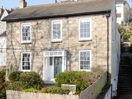 A stone house with a green door and white framed windows surrounded by bushes and a wooden fence at Belmont in Newlyn