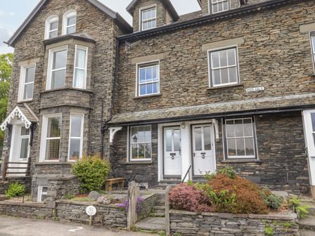 Stone exterior of a two story house with white doors and windows and a small garden at Primrose Cottage in Ambleside