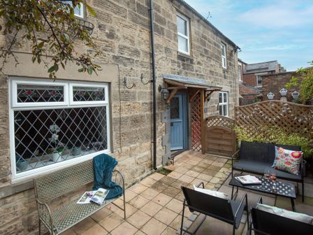 A stone exterior patio with metal and black chairs a wooden bench and a blue door at Owl Cottage in Morpeth