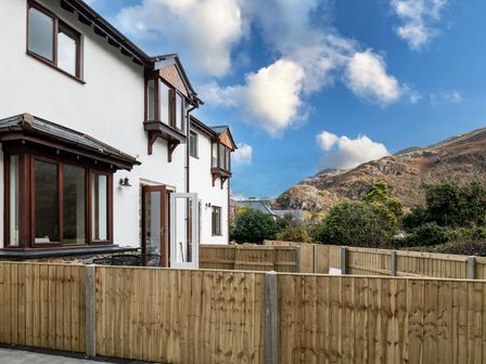 A row of white houses with brown framed windows and wooden fences in front with hills in the background at Hebog in Beddgelert