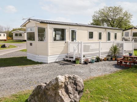 A beige mobile home with white railing and potted plants outside on a gravel path at The Maples in Steel Green near Haverigg