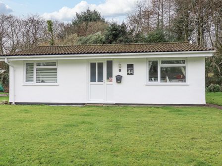 A white single-story house with two windows and a door in the center surrounded by grass at Merryfield Lodge in Rosecraddoc near Liskeard