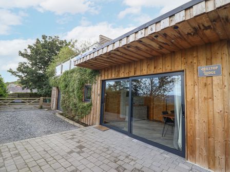 The exterior of a wooden building with large sliding glass doors and a gravel driveway at Hilltop Lodge in Corwen
