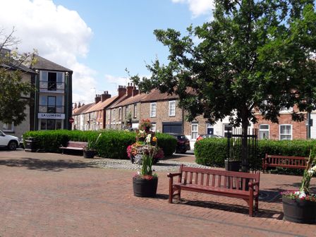 A small urban park with benches flower pots a tree and residential buildings in the background at No.37 in Beverley