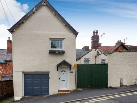 A detached house with a white door and grey garage door beside a green wooden gate on a sloped street at Dove Cottage in Ruthin