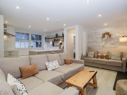 A living room with two beige sofas a wooden coffee table and an open kitchen area at Dixon Court in Ambleside