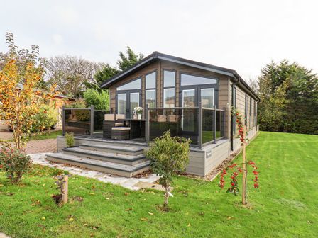 A cabin with a wooden deck and outdoor seating in a garden with small trees and grass at Hideaway Lodge in Runswick Bay