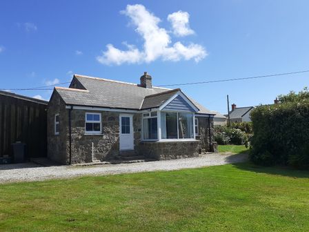 A stone cottage with a gravel driveway and a lawn under a blue sky at Wellfield Cottage in Sennen