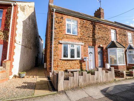 A stone brick end terrace house with a white door and wooden fenced garden at 57 Southend Road in Hunstanton