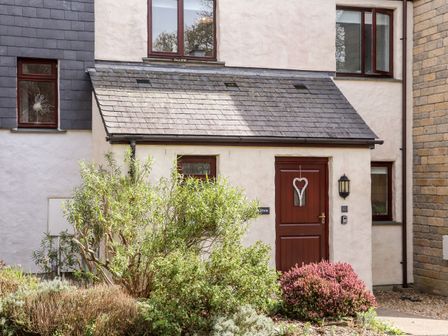 A house entrance with a wooden door and plants in front at Charleston Cottage in Falmouth