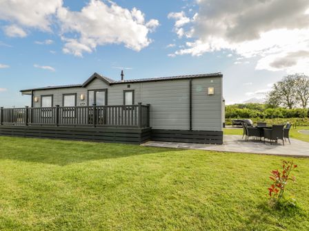 A grey mobile home with a deck and outdoor dining set on a lawn at Happy Daze Carnaby near Bridlington