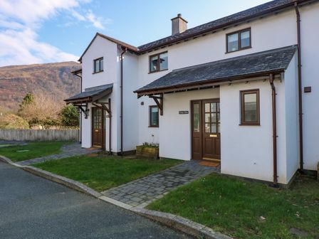 A driveway and path leading to two front doors of attached houses with grassy lawns and hills in the background at Craig y Llan in Beddgelert