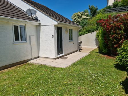 A house with white walls a black door and windows a satellite dish on the roof and a garden with grass and shrubs at Waters Reach in Kingsbridge