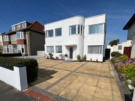 A white two-story house with large windows and a paved driveway with plants on the sides at The Emberton in Bridlington