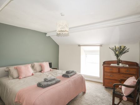 A bedroom with a double bed pink pillows and blanket a wooden dresser with flowers and a wooden chair at Cwm Ceiliog Annex Llanaelhaearn near Trefor