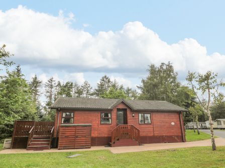A wooden cabin with a small porch and stairs surrounded by grass and trees at 4 The Oaks in Swarland