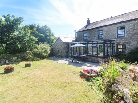 A garden with grass flowers and picnic table outside a stone house at Trevedran Cottage in St Buryan