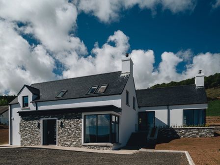 A modern two-story house with stone and white exterior walls under a blue sky at Lamb Cottage in Ballycastle