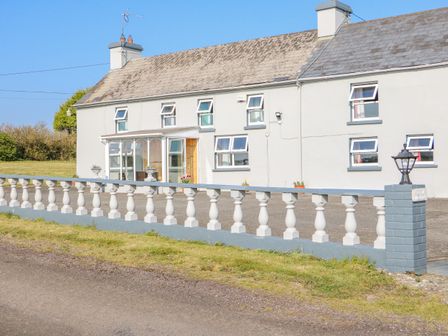 A white house with multiple small windows and a glass porch behind a white balustrade fence at Gleann Griannmhar in Ballyoughtera near Rosscarbery County Cork