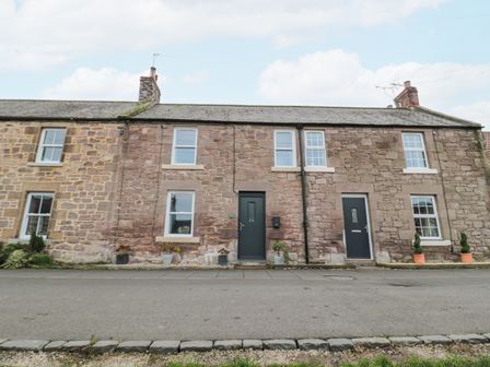 A row of stone houses with dark front doors and several windows at Castle Keep in Norham
