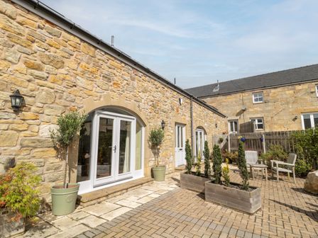 An outdoor patio area with stone walls potted plants wooden planters and chairs at Calm Skies in Scremerston near Berwick-Upon-Tweed