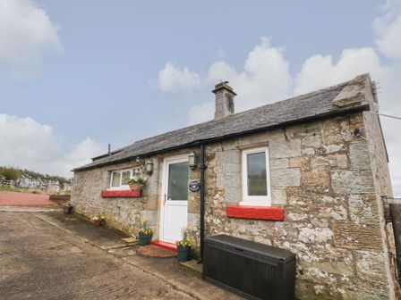 An exterior view of a stone cottage with flower pots near the door and red window sills at Healey Farm Cottage in Rothbury