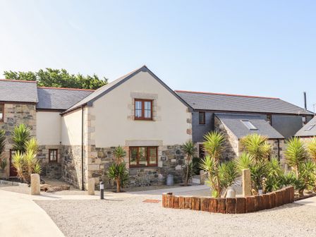 A stone and stucco house with small plants and gravel in front at Polurrian House in Cury near Mullion