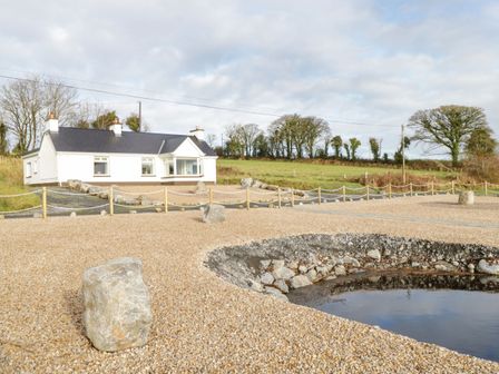 A white house with chimneys near a gravel area and a small pond with rocks at The Waters Edge in Boyle County Roscommon