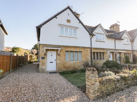 A stone and white exterior of a cottage with a gravel driveway and a garden at Dazie Cottage in Broadway