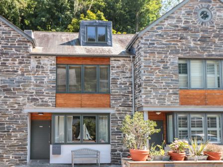 A stone exterior of a townhouse with windows a wooden bench and potted plants at 6 Pottery Cottages in Dartmouth