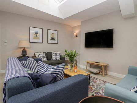 A living room with blue and gray sofas a wooden coffee table and a wall mounted TV at Helton Fell in Kendal