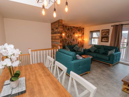 A living room with teal sofas a wooden dining table and floral wallpaper at Whitby Haven in Whitby