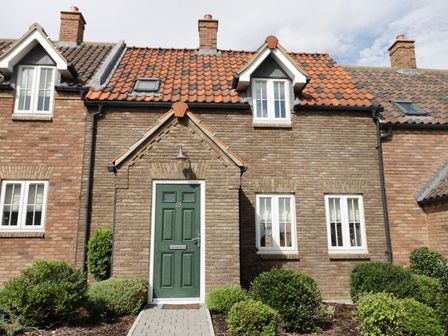 Front view of a brick house with green door and white framed windows with bushes in front at Meadow View in Filey