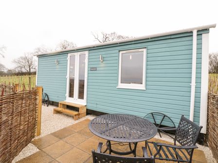 An outdoor patio with a round metal table and chairs next to a blue wooden cabin at Robins Nest in Napton-On-The-Hill