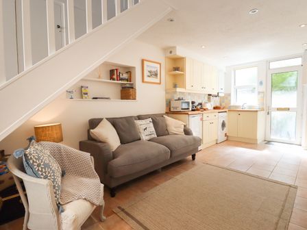 A living area with a gray sofa and white armchair next to a small kitchen at Quayside Cottage in Teignmouth