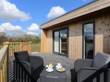 An outdoor wooden deck with black wicker chairs and a table with coffee cups and cakes at The Swift in Wem