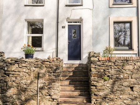 Stone steps leading to a blue front door of a white house with stone walls and windows on either side at 9 Ty Du Road Llanberis
