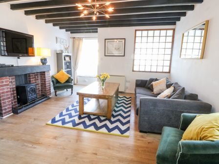 A living room with a gray sofa green armchairs a wooden coffee table and a fireplace at Malltraeth Cottage in Malltraeth