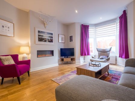 A living room with purple curtains a magenta armchair a gray sofa and a wooden coffee table at Howe Keld 2 Ground Floor Keswick