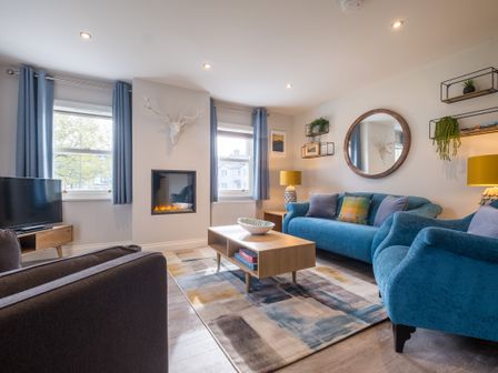 A living room with blue sofas a wooden coffee table a wall-mounted fireplace and a wall mirror at Howe Keld 3 Ground floor in Keswick