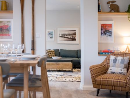 A dining area with wooden table and chairs next to a living room with a green sofa a wooden coffee table and framed pictures on the wall at Howe Keld 5 First Floor in Keswick