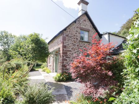 Stone cottage with green door and windows surrounded by garden plants and trees at Caldhu Cottage in Holmrook