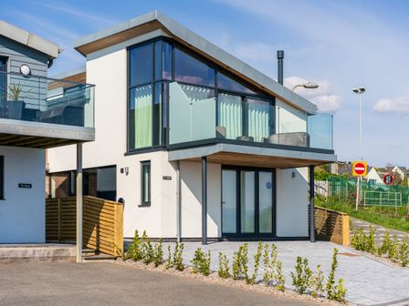 A modern two-story house with glass balcony and patio doors at Ty Mor in Criccieth