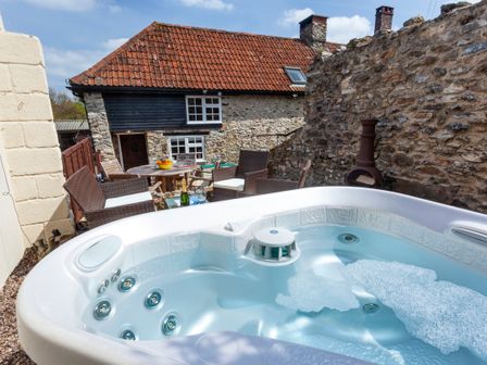 An outdoor patio with a hot tub wicker chairs a round table and a stone building at Southcott Farm Cottage in Sheldon
