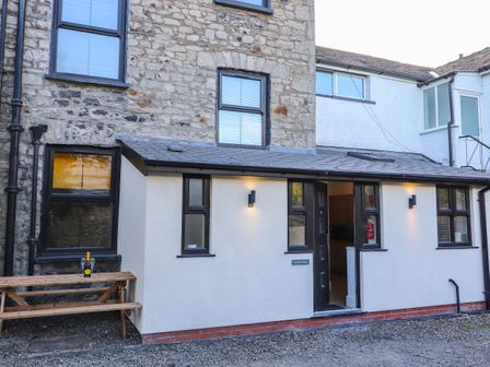 Exterior view of a stone and white rendered building with black framed windows a wooden bench with a bottle and glasses Aryelle House Kendal