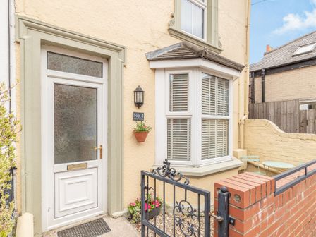 Front entrance of a house with a white door and bay window with shutters at Postmans Cottage in Bridlington