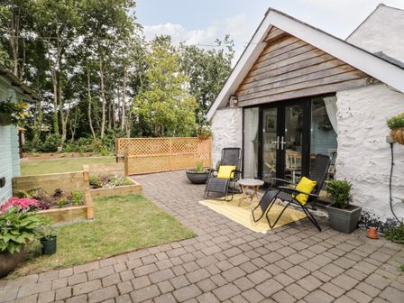 A patio with two chairs and a small table outside a white house with glass doors and raised flower beds at The Old Stable in Henryd near Conwy
